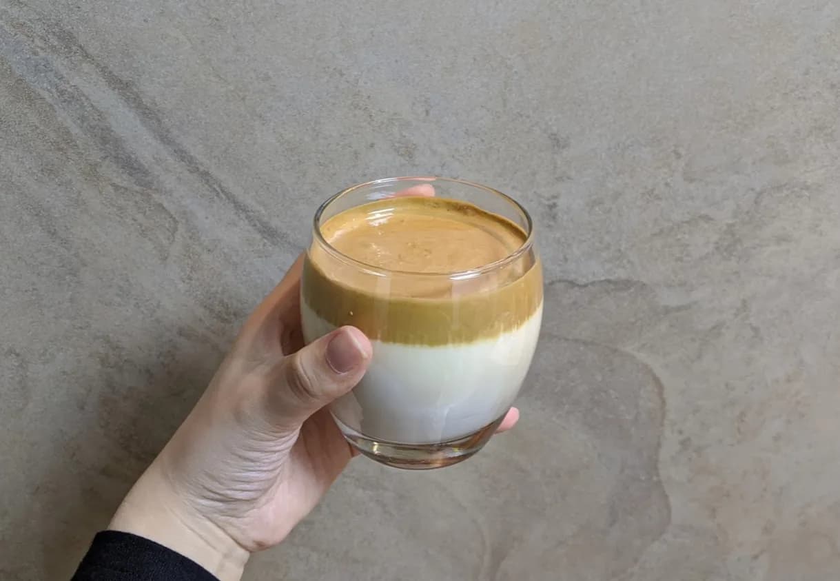 A hand holds a glass of milk topped with whipped coffee foam, photographed for Google’s dalgona trend report.