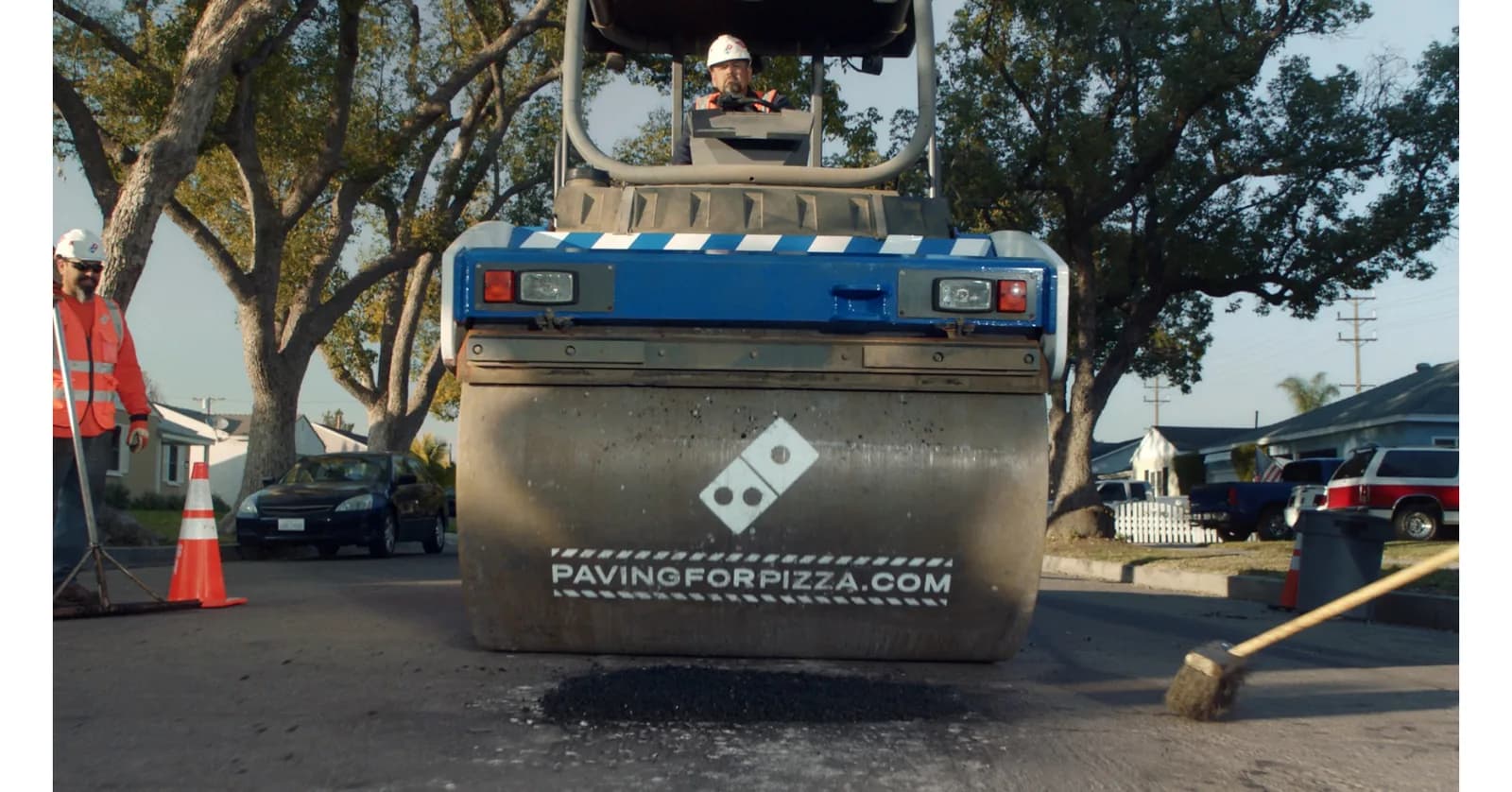 A Domino’s-branded road roller and crew at a Paving for Pizza repair.