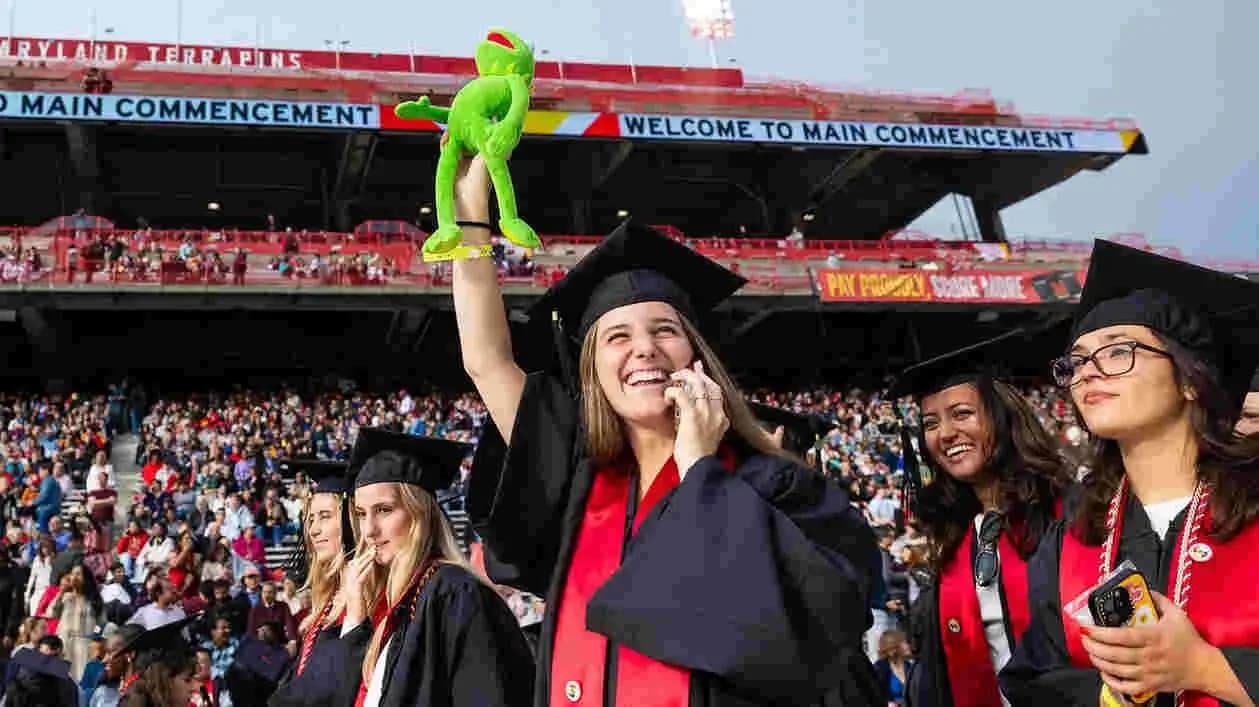 Official UMD commencement coverage, with graduates holding Kermit dolls at SECU Stadium.