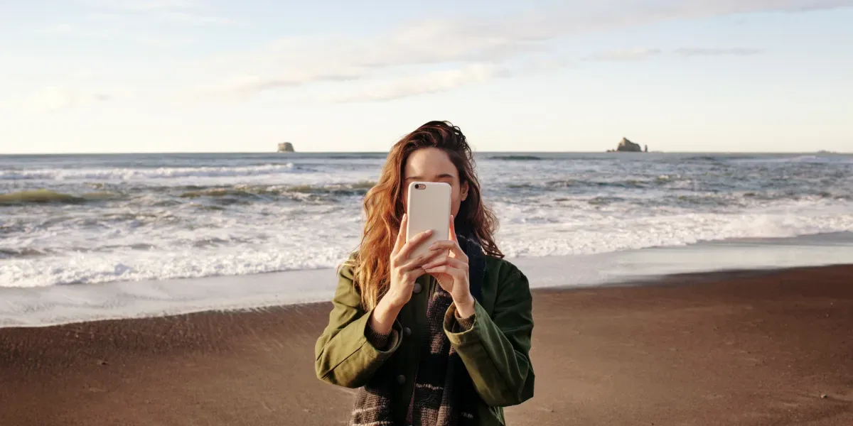 A young woman takes a picture with her phone on the beach.