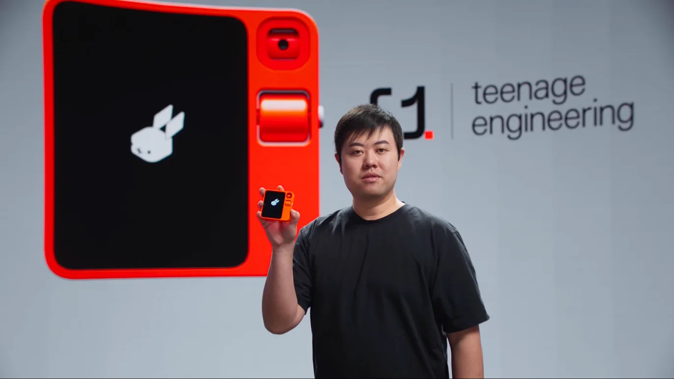 a person on stage holding an r1 in front of a rabbit and teenage engineering backdrop