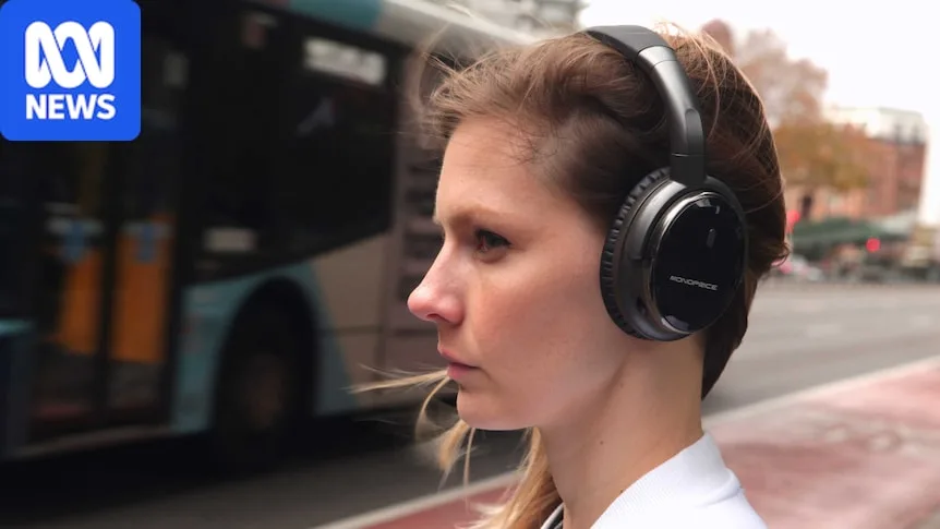 A woman stands next to a busy street while wearing headphones.