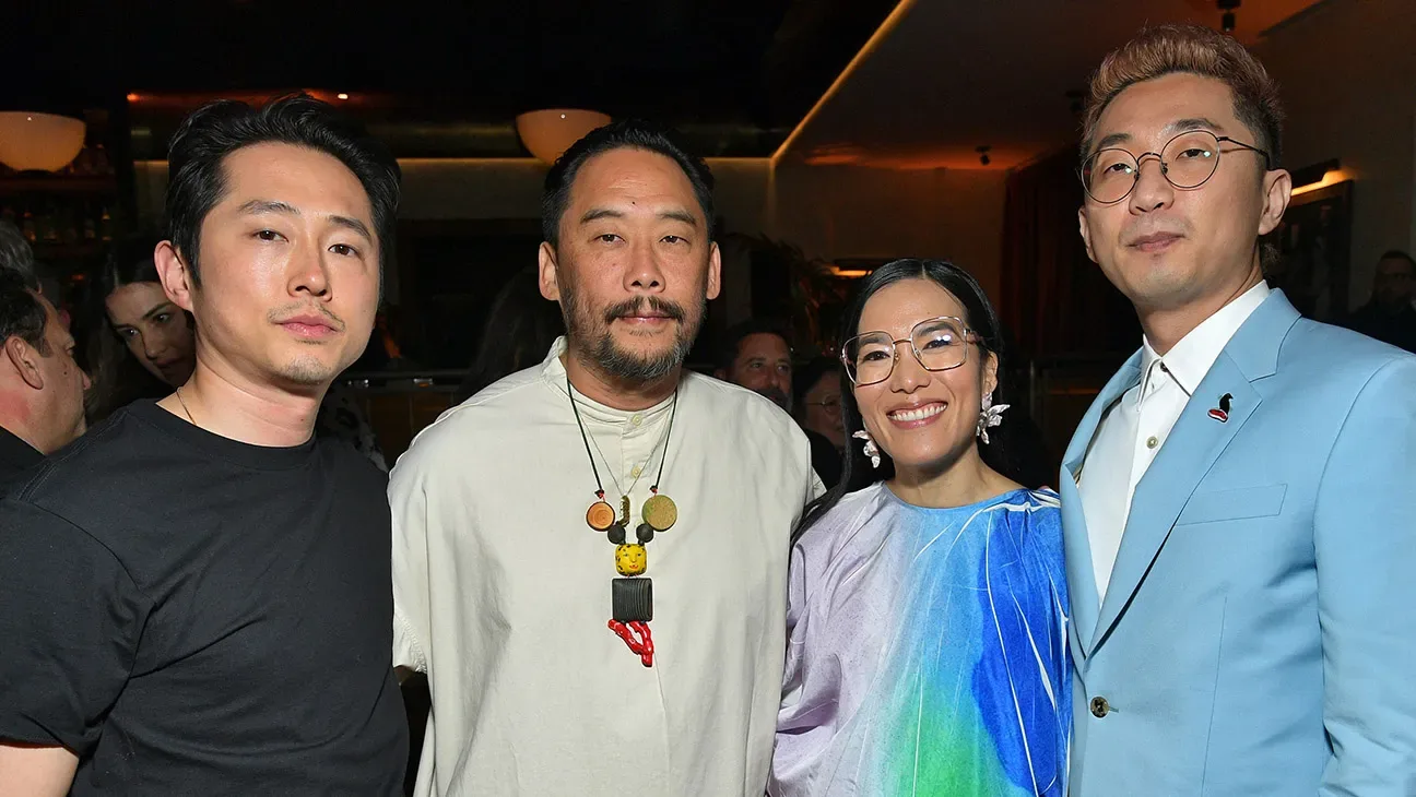 Steven Yeun (black T-shirt), David Choe (white T-shirt with colorful wooden pendant necklace), Ali Wong (blue, green and white dress) and Lee Sung Jin (light blue suit) pose together for a photo.