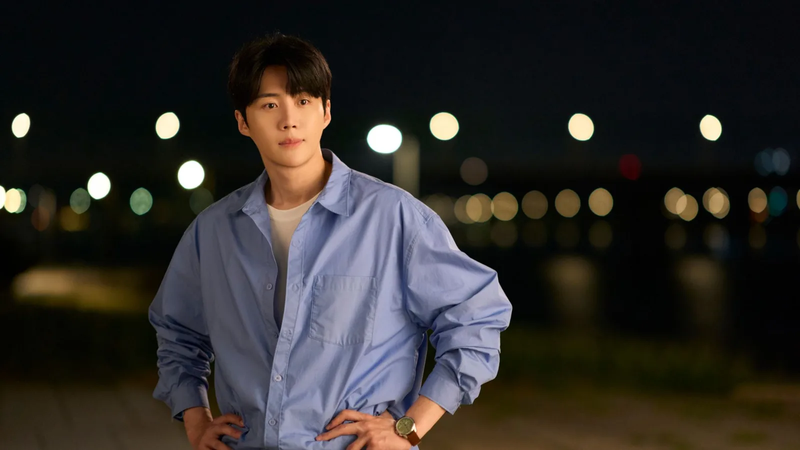 A man in a blue button-down (Kim Seon-ho as Joo Ho-jin) stands on a beach at night, in the Netflix K-drama 'Can This Love Be Translated?'