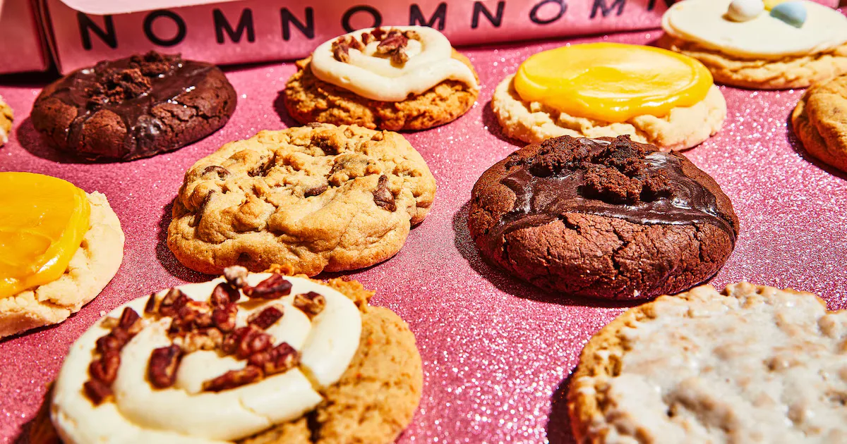 Crumbl's oversized cookies on a pink 'nom nom nom' backdrop.