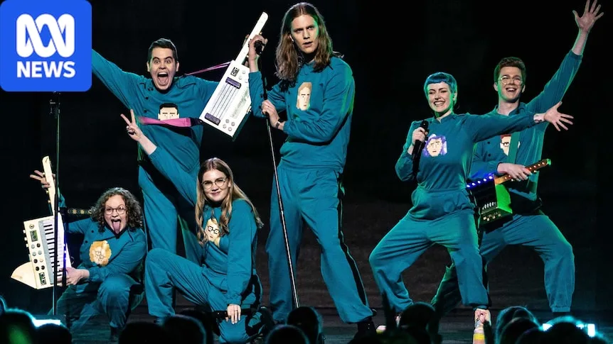 Six-piece band Daði & Gagnamagnið are seen in matching blue tracksuits against a black backdrop. Some hold synth instruments.