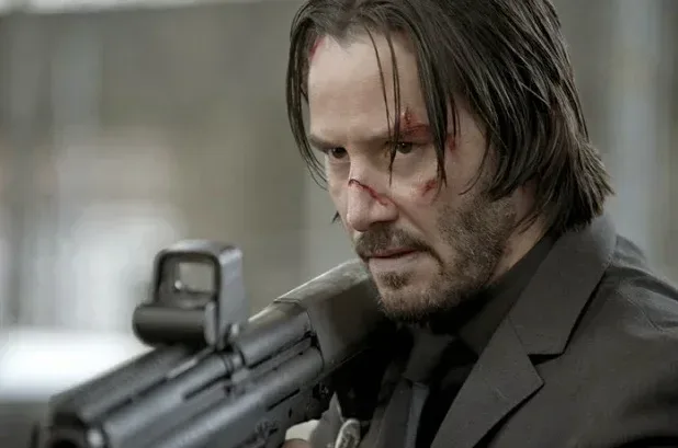 Keanu Reeves as John Wick, aiming a rifle