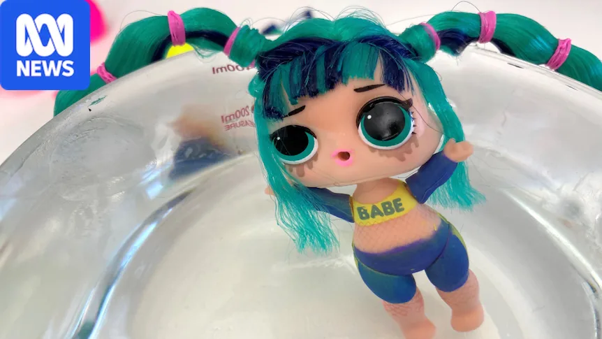 A small plastic doll sitting in bowl of water with bike pants and a top with "babe" written across it.