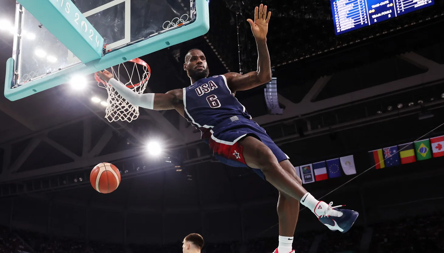 Lebron James, wearing a blue "Team USA" uniform, is shown midair as he dunks the ball during an Olympic basketball game.