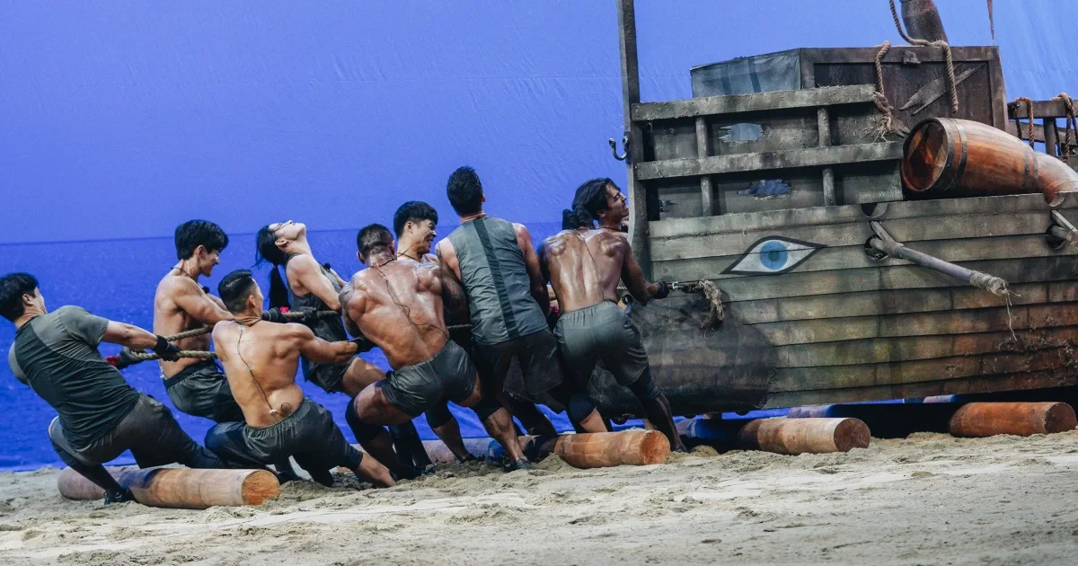 Teams haul a ship across the beach in a Physical: 100 tug-of-war