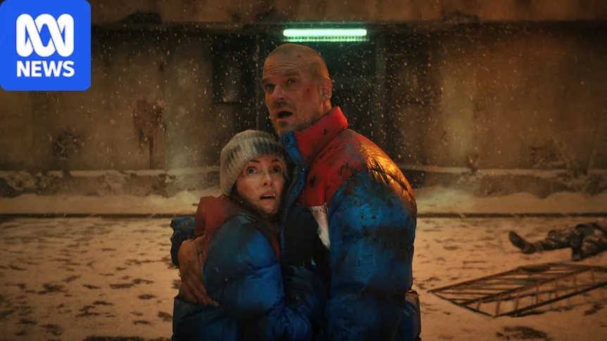 A bloody and brusied couple embrace in a snowy prison courtyard