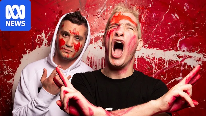 Two brothers stand gesturing with their hands while covered in red paint