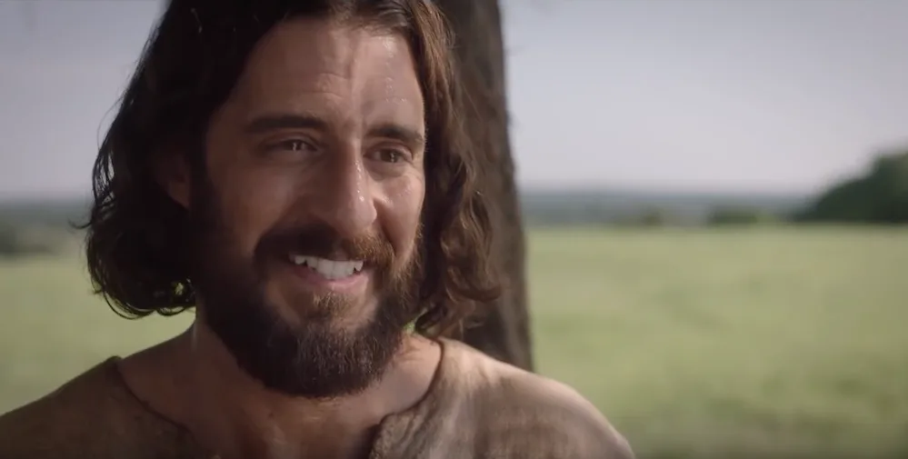 Jonathan Roumie as Jesus smiling in a field