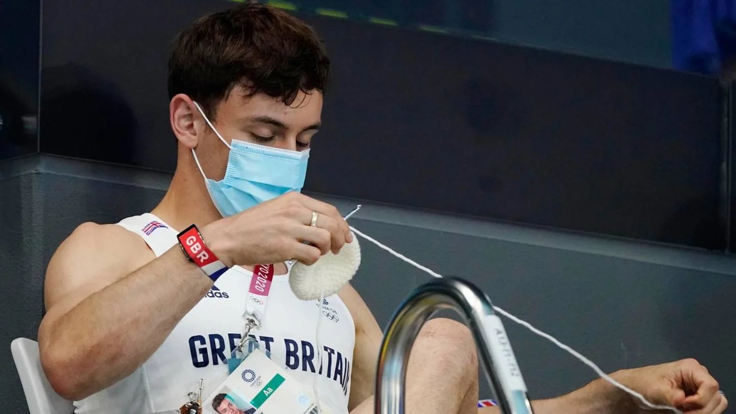 Daley, masked, knits poolside in Tokyo