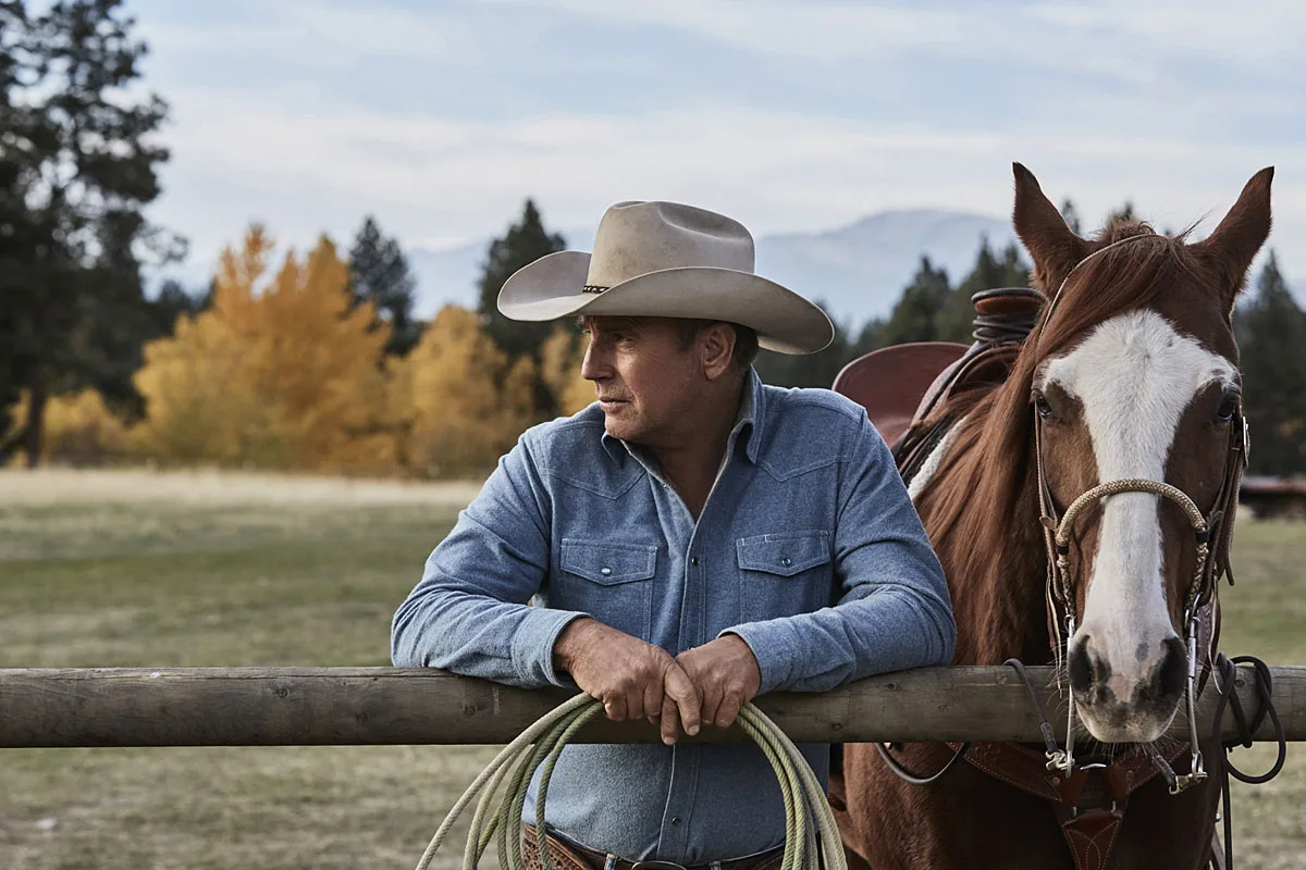 Kevin Costner leaning on a fence beside a horse